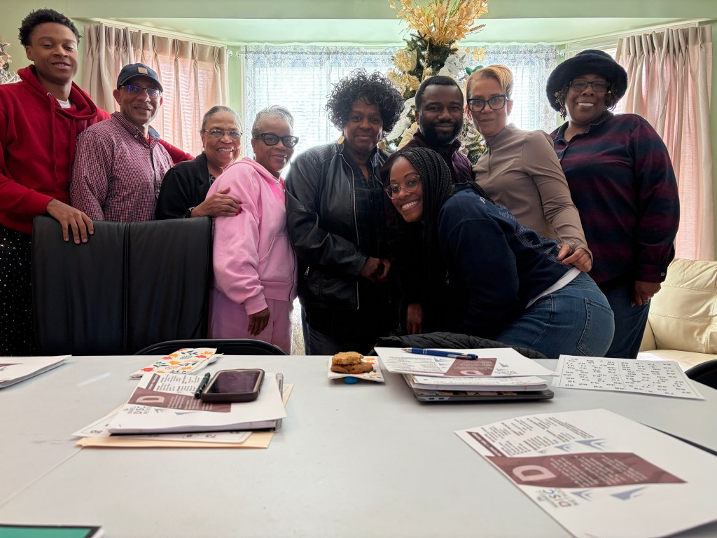 Group photo of workshop participants posing together in a light-filled room with decorative elements, including a plant, showcasing a sense of community and collaboration.